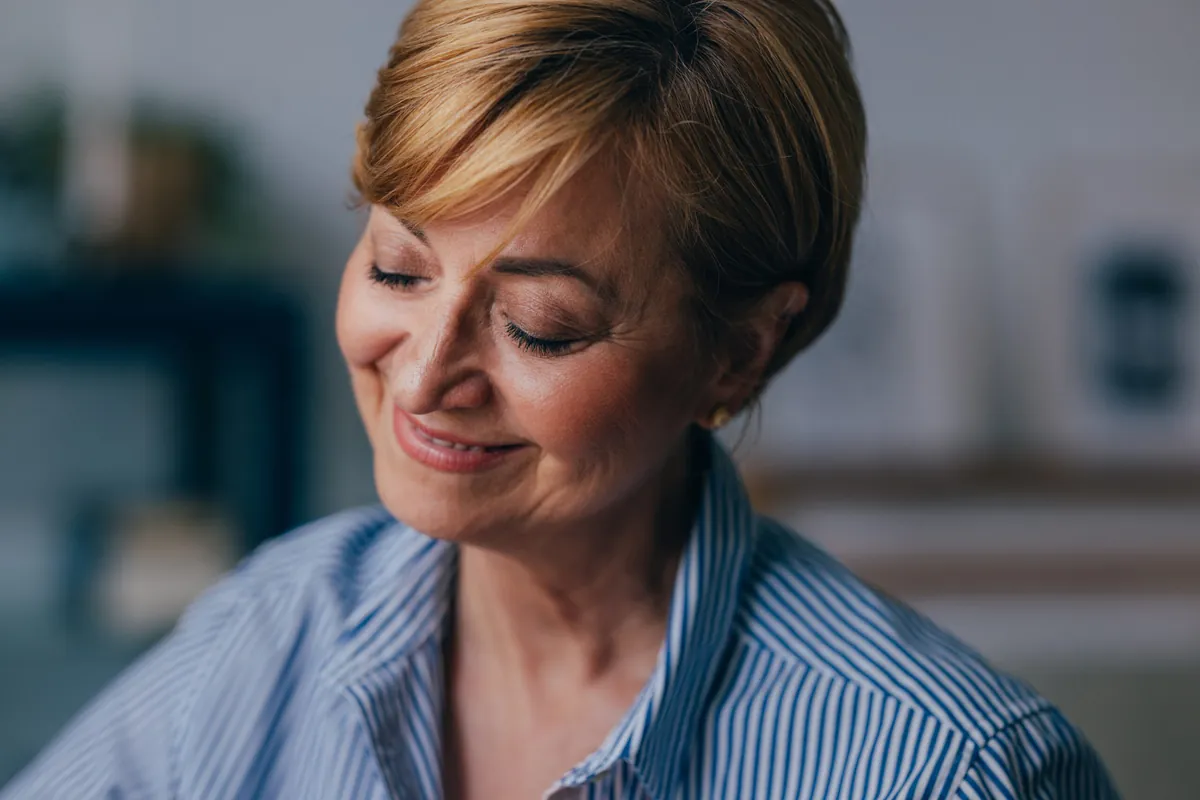 A pensive Caucasian female looking down smiling and relaxing while thinking about something nice.