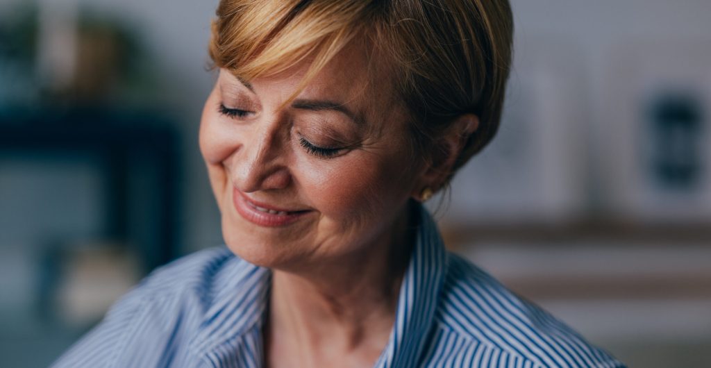 A pensive Caucasian female looking down smiling and relaxing while thinking about something nice.