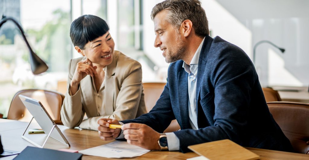Two business people are discussing a project in a modern office, using a digital tablet and paperwork